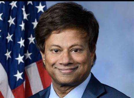 A man in a suit and tie is smiling in front of an American flag.
