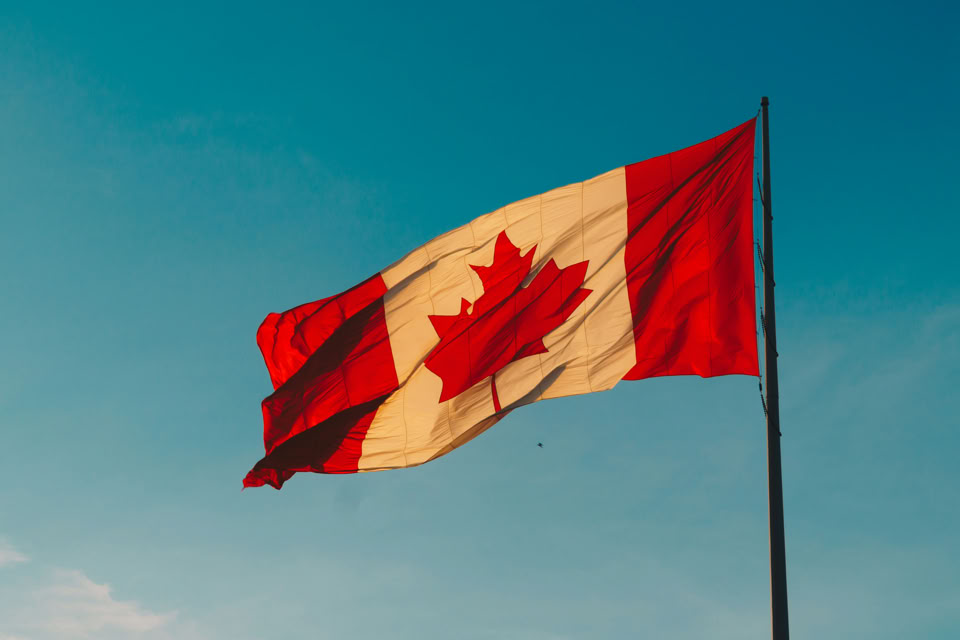 A Canadian flag waving against a clear blue sky.
