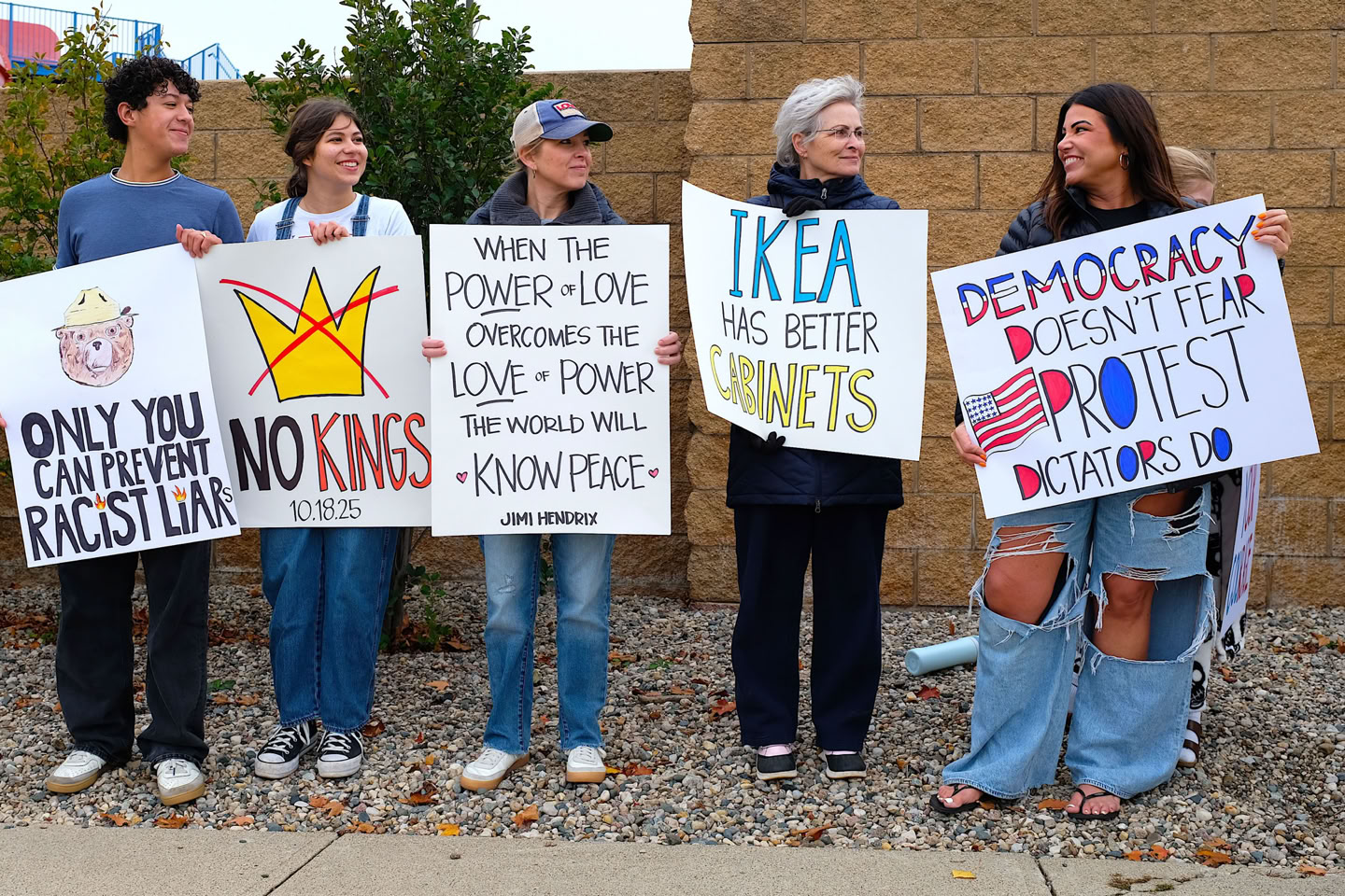 Five people standing outdoors holding protest signs with various messages.