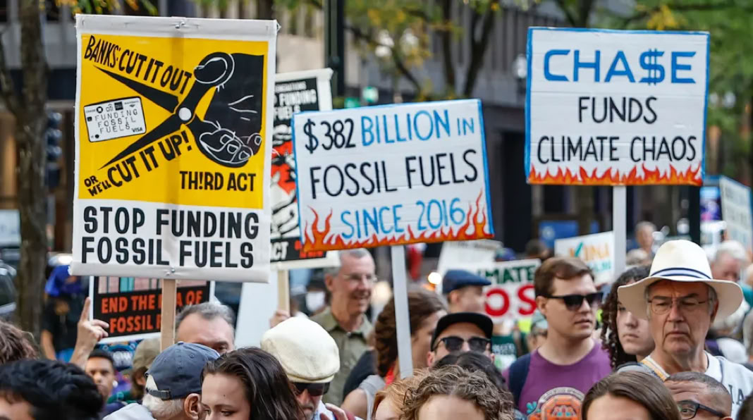 A group of people holding signs at a protest, with messages about stopping fossil fuel funding and climate change.